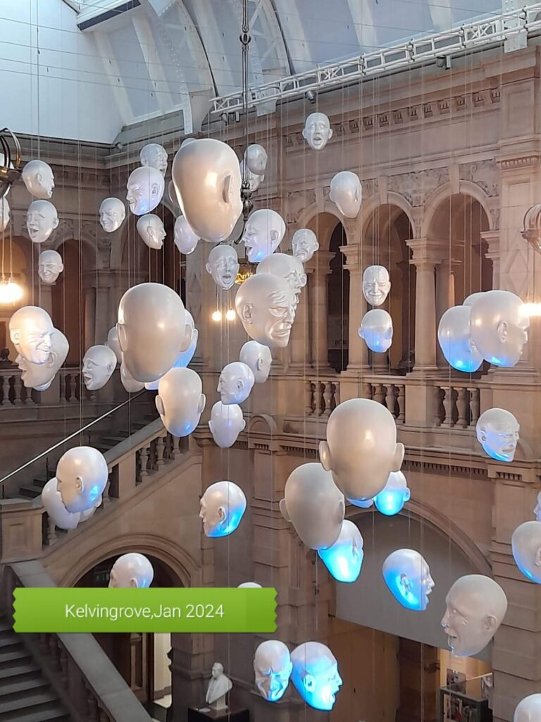 The internior of a large hall in Kelvingrove museum with sculpted faces hanging from the ceiling